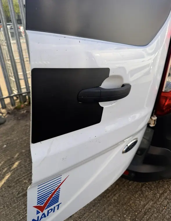 Black handle-area repair plate on rear door of white Ford van